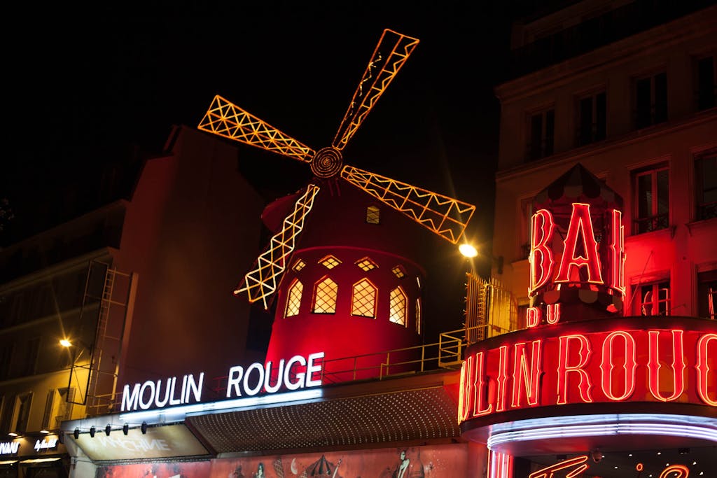 Brightly illuminated Moulin Rouge windmill in Paris at night.
